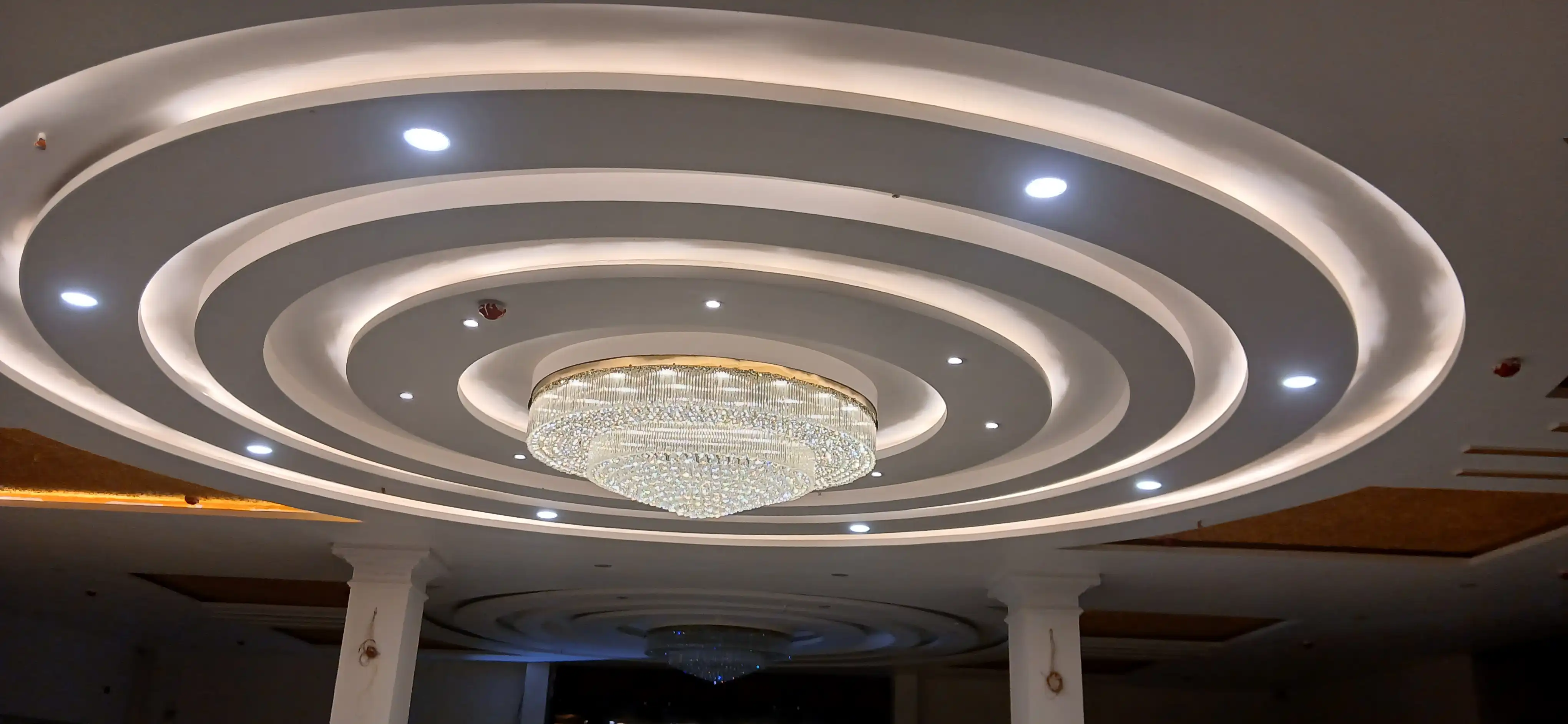 Modern round crystal chandelier installed in a grand circular false ceiling
