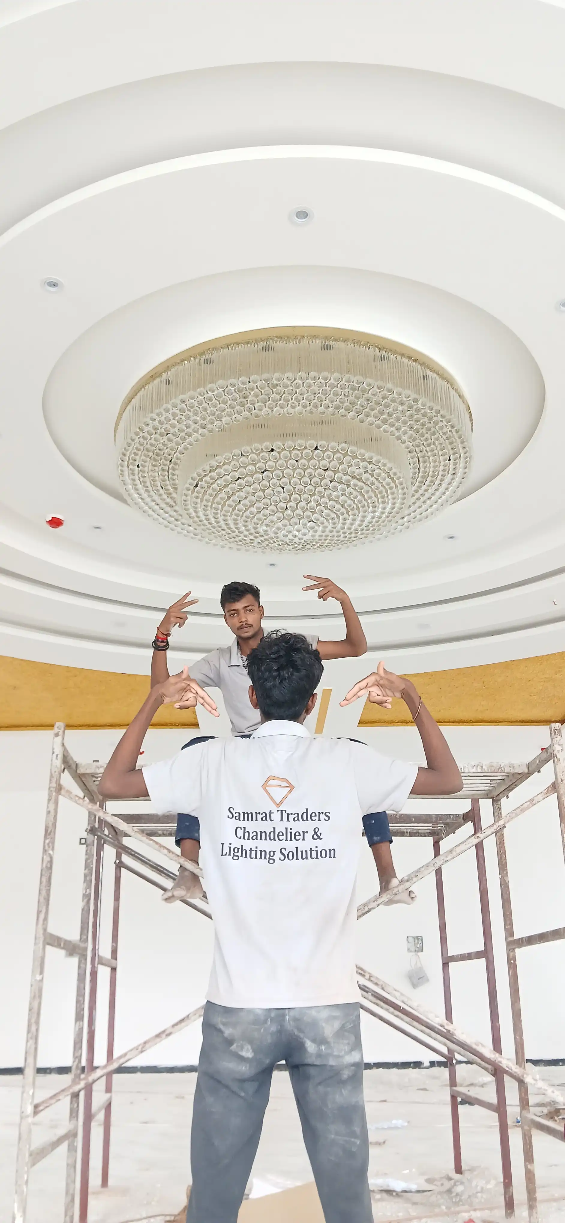 Samrat Traders team installing a large round crystal chandelier in a grand banquet hall
