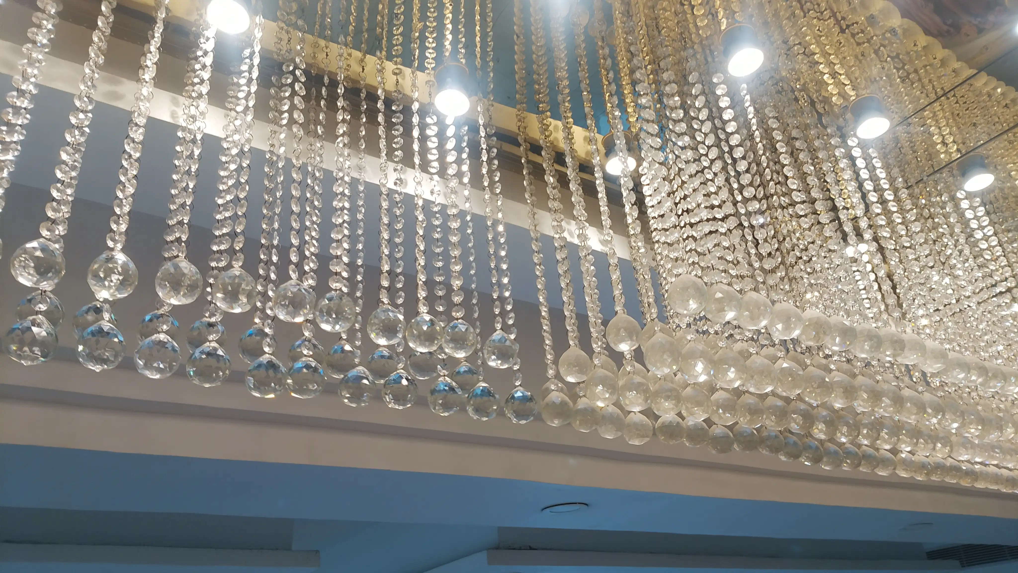 Before and after chandelier cleaning showing clean and dusty crystal sections in a banquet hall