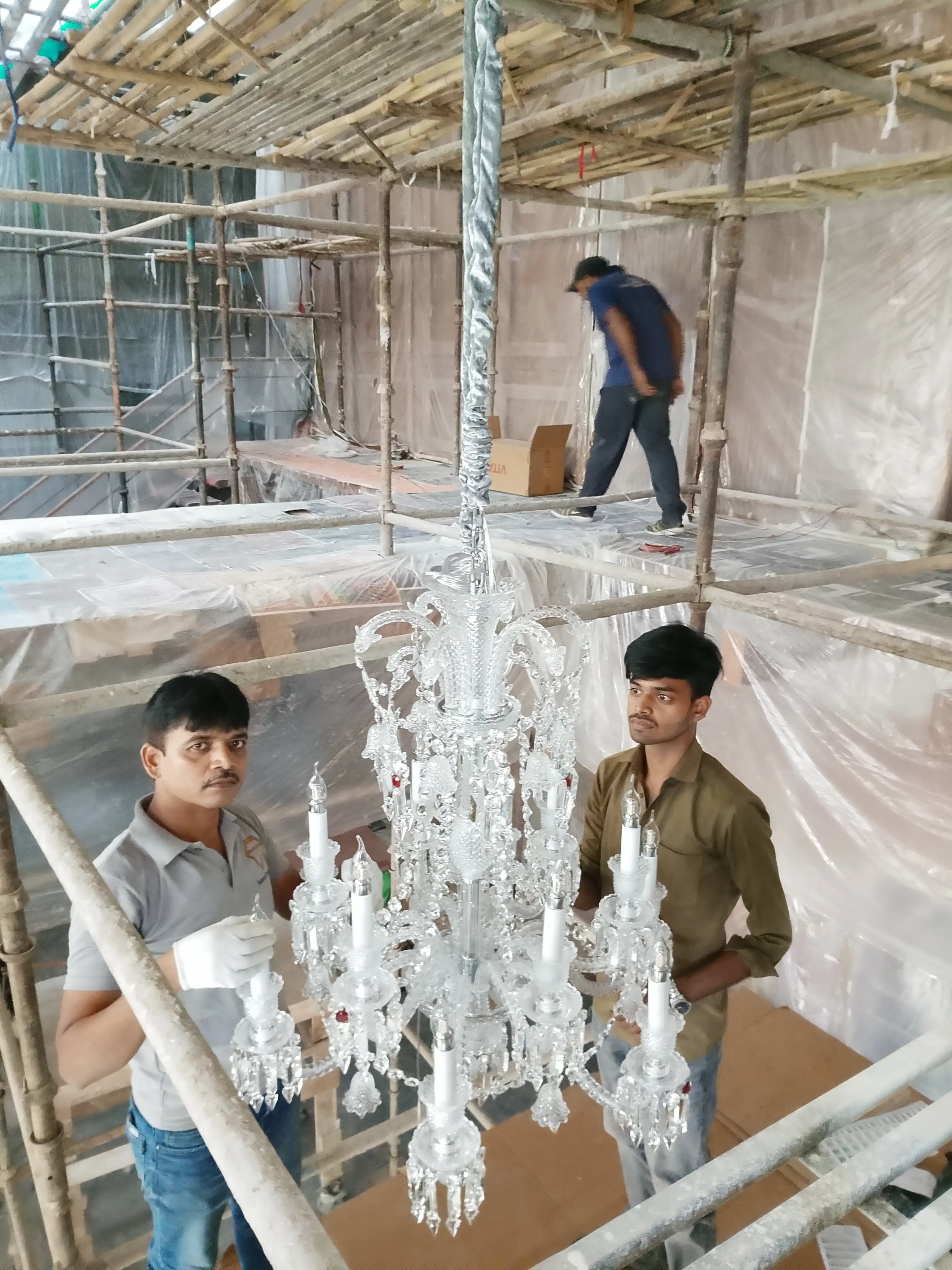 Large imported crystal chandelier being installed by Samrat Traders team at a luxury interior project